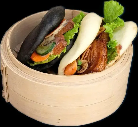 A black bao and a white bao filled with pork, lettuce, carrot and cucumber in a bamboo steamer